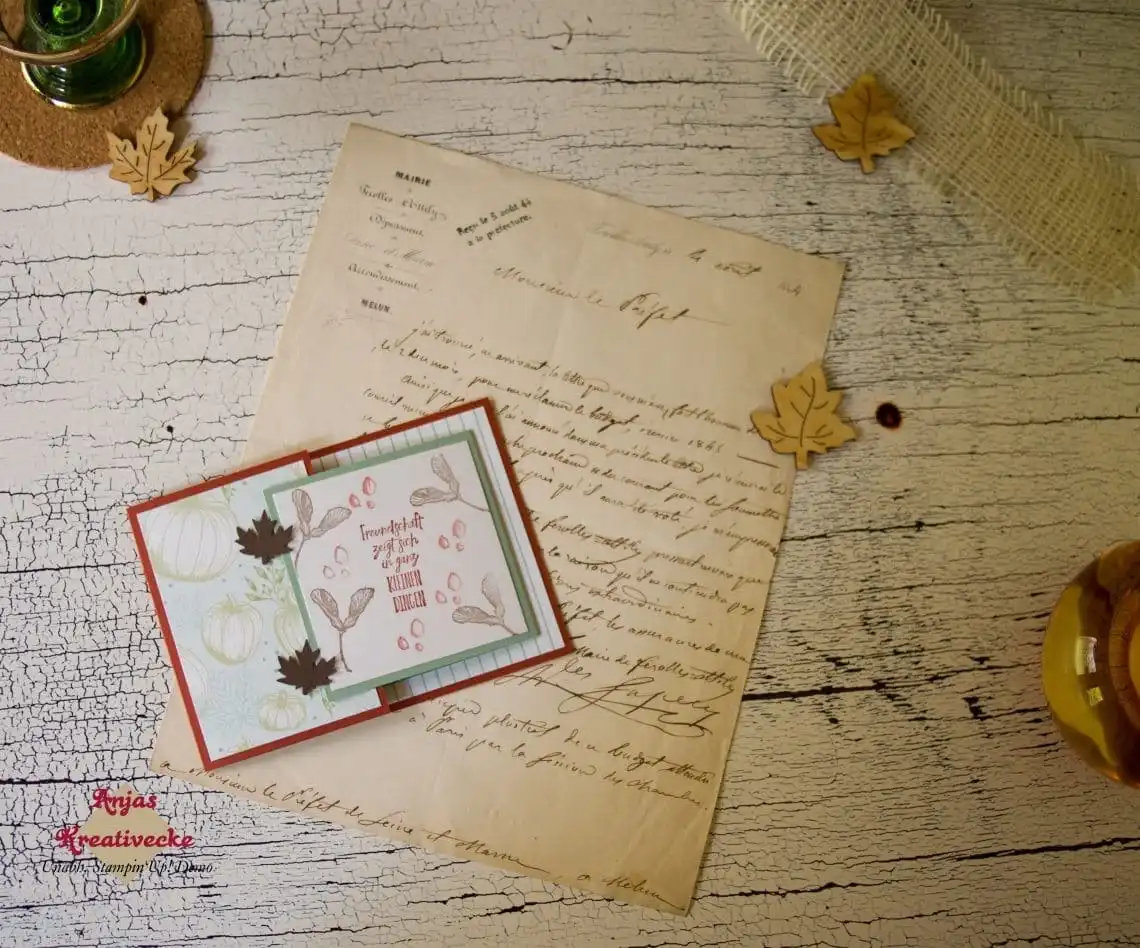 Flatlay der geschlossenen Joy-Fold-Karte mit Kürbis-Designerpapier und Ahornblättern auf altem Schriftstück