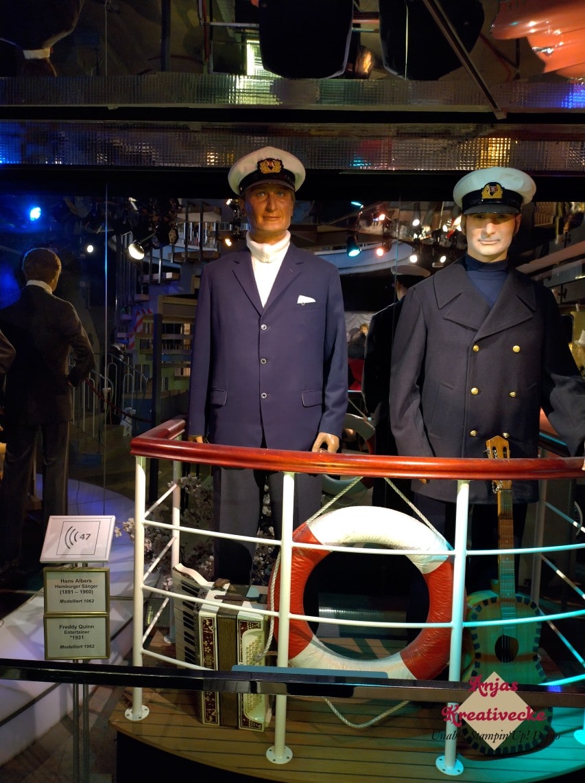 Die Wachsfiguren von Hans Albers und Freddy Quinn auf einem Boot mit rot-weißem Rettungsring. Beide tragen Anzug und Kapitänsmütze.
