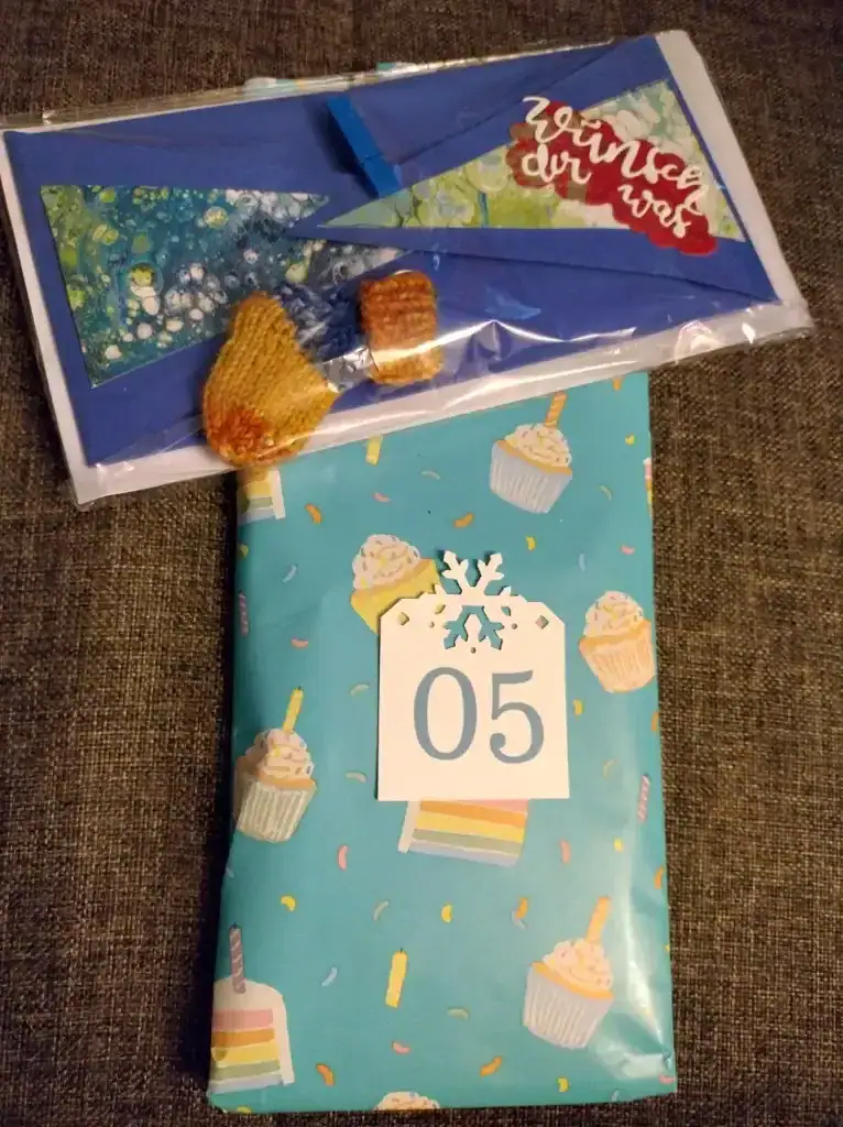 Kreativprojekte Adventskalendertausch Karte mit zwei waagerechten Spitzen in Blau, zusammengehalten von einer kleinen Wäscheklammer. Als Beigabe liegt eine kleine gestrickte Socke als Schlüsselanhänger dabei. Gestaltet von Miriam